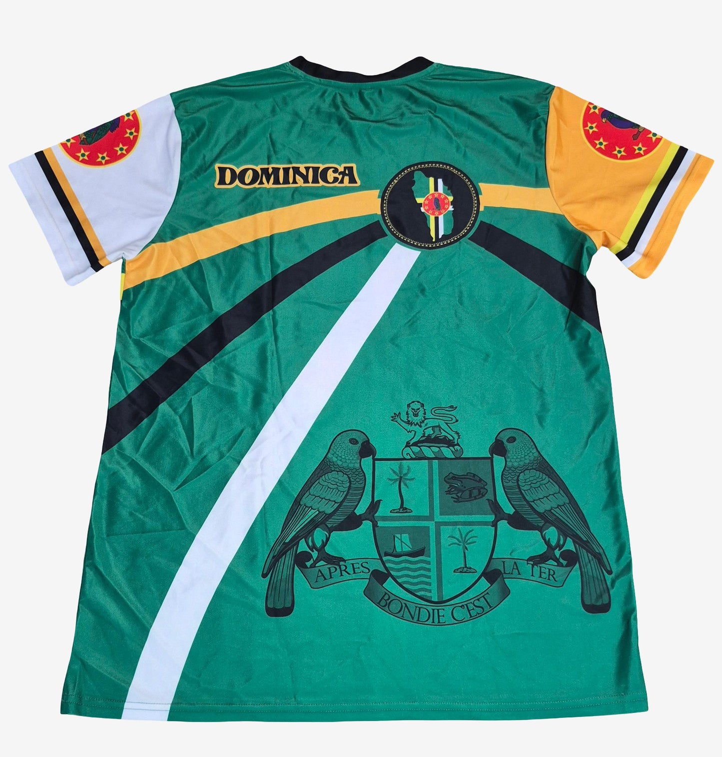 A green short-sleeve soccer jersey with Dominica graphics, featuring the word 'DOMINICA' on the chest, a central crest, and the national coat of arms with two parrots on the back. The sleeves have white and yellow sections with red and black details.