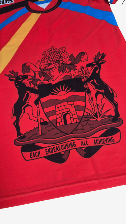 Close-up of a red sports jersey featuring a large black and red provincial coat of arms graphic with the motto 'EACH ENDAVOURING ALL ACHIEVING' across the front.